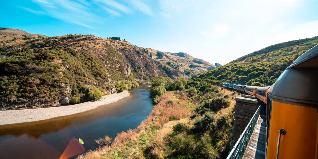 Scenic view from the Taieri Gorge Railway as it travels through rugged hills beside a winding river in Dunedin.