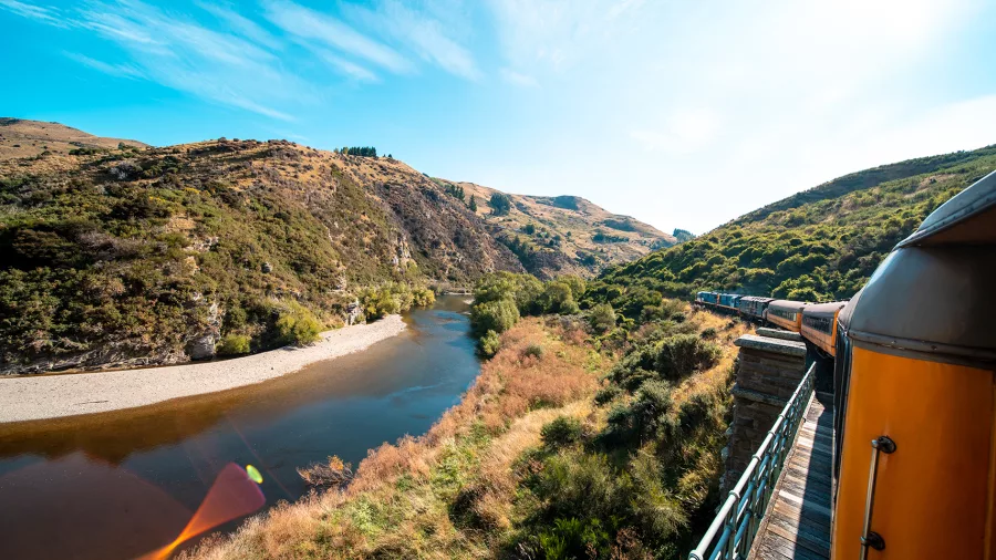 Scenic view from the Taieri Gorge Railway as it travels through rugged hills beside a winding river in Dunedin.