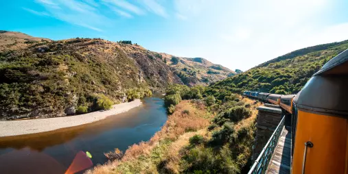 Scenic view from the Taieri Gorge Railway as it travels through rugged hills beside a winding river in Dunedin.