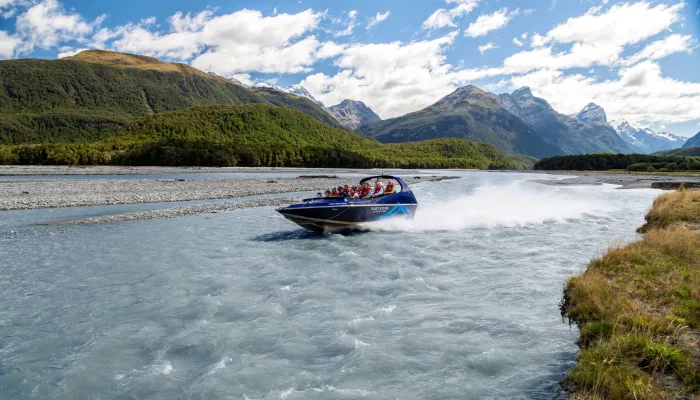 Jet boat speeding along the braided Dart River in Glenorchy with scenic mountains behind.
