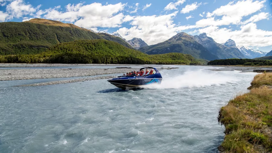 Jet boat speeding along the braided Dart River in Glenorchy with scenic mountains behind.