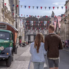 Couple walking through Oamaru Victorian Precinct in Waitaki, New Zealand, past heritage buildings and a vintage green truck.