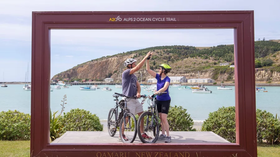 Cyclists high-fiving at the end of the Alps 2 Ocean Cycle Trail in Oamaru, New Zealand.