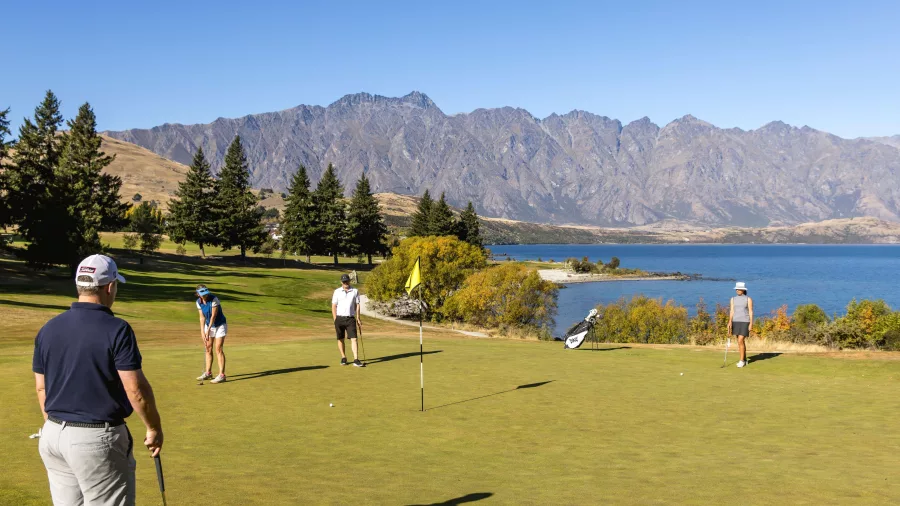 Golfers on the putting green at Queenstown Golf Club beside Lake Wakatipu with mountain views