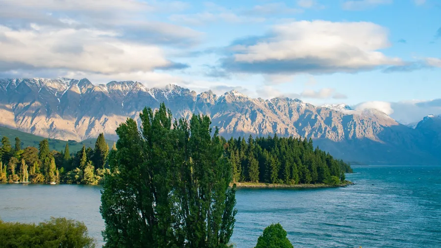 View of the Remarkables mountain range from the Queenstown lakefront with trees in the foreground