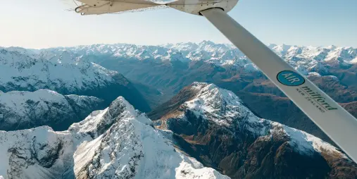 View from a Cessna aircraft wing flying above glacier-covered peaks in the Southern Alps