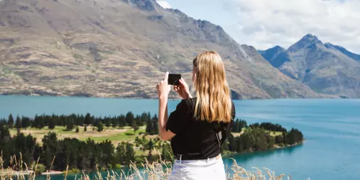 Visitor taking a photo of Lake Whakatipu and the surrounding mountains from a high vantage point near Queenstown