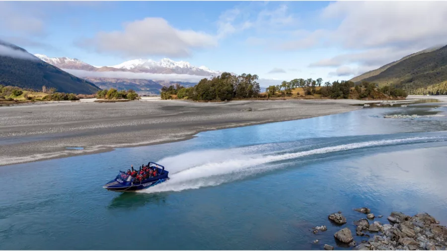 Jet boat speeds down the Dart River near Glenorchy with snow-capped mountains in the background.