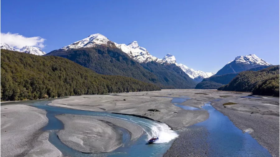 Dart River jet boat cutting through a wide glacial riverbed under a clear blue sky.