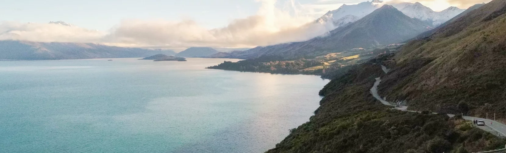 Tour van driving along the Glenorchy-Queenstown Road with views over Lake Wakatipu and distant mountains