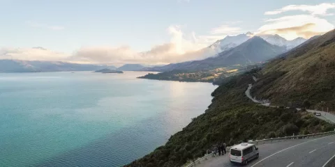 Tour van driving along the Glenorchy-Queenstown Road with views over Lake Wakatipu and distant mountains