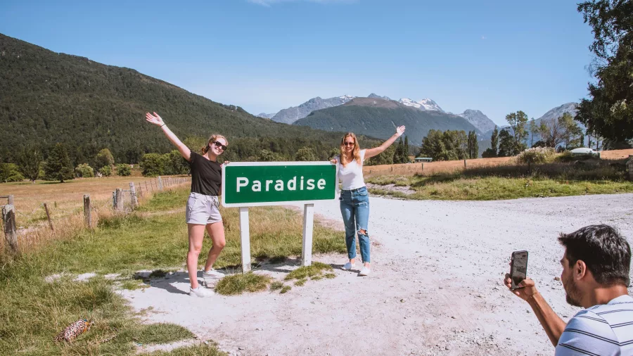 Two women posing at the Paradise sign near Glenorchy while another takes a photo