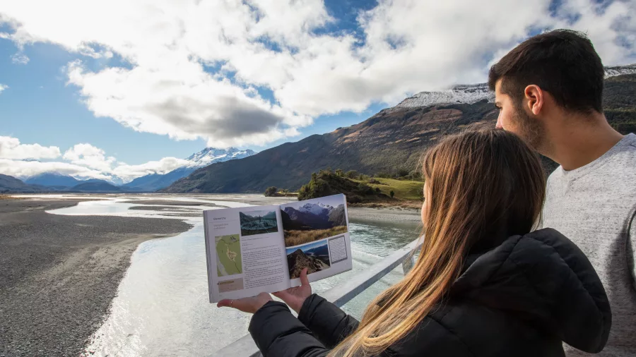 Couple holding a film location guide while looking over braided rivers and mountains near Glenorchy