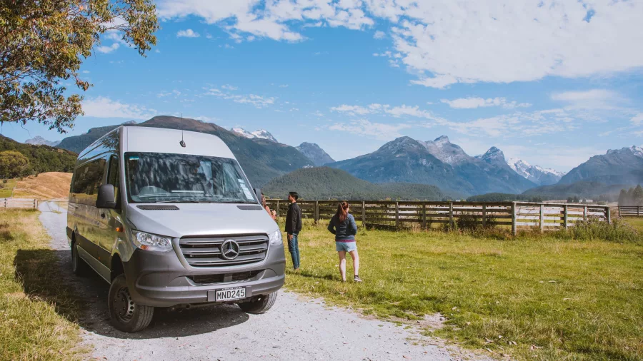 Small group tour van parked on a gravel road near Glenorchy with travellers admiring mountain views