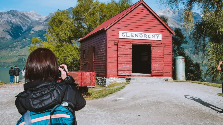 Visitor taking a photo of the historic red Glenorchy boatshed near Lake Wakatipu