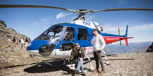 Couple relaxing by a helicopter on a Queenstown luxury wine tour
