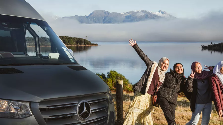 Travellers posing near an Altitude Tours van at Te Anau Downs with lake and mountains behind