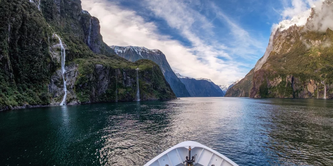 View from the front of a cruise boat sailing through the fjord in Milford Sound with waterfalls and cliffs