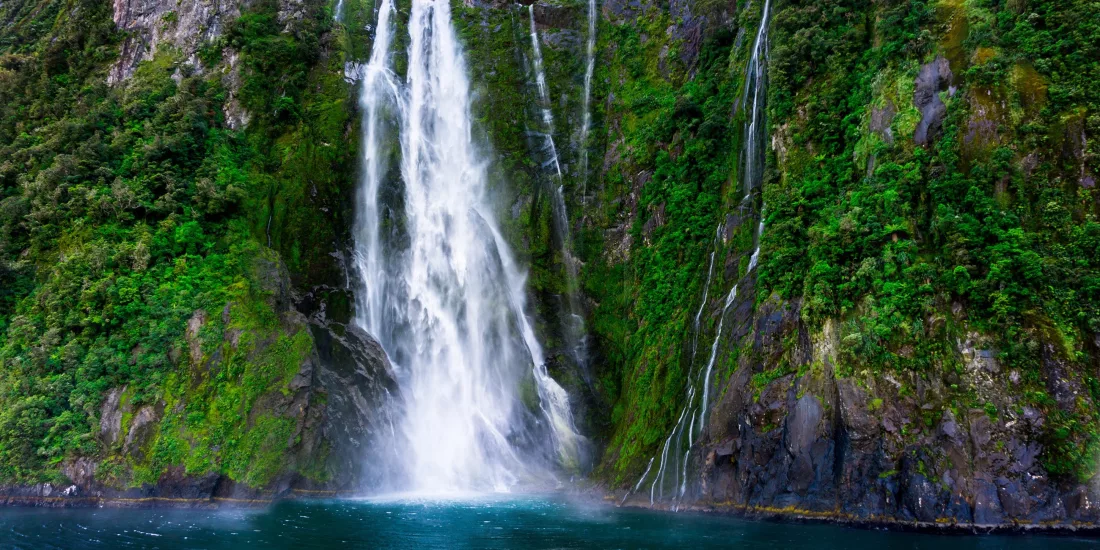 Stirling Falls cascading down lush cliffs into the fjord on a Milford Sound cruise