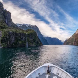 View from the front of a cruise boat sailing through the fjord in Milford Sound with waterfalls and cliffs