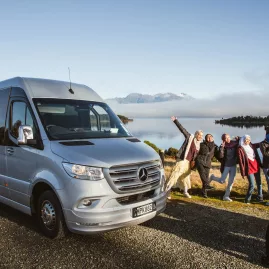 Small group tour guests posing by a premium van at a scenic stop on the way to Milford Sound
