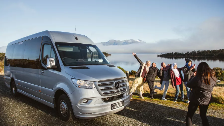 Small group tour guests posing by a premium van at a scenic stop on the way to Milford Sound
