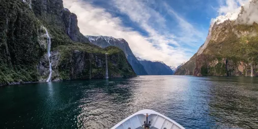 View from the front of a cruise boat sailing through the fjord in Milford Sound with waterfalls and cliffs