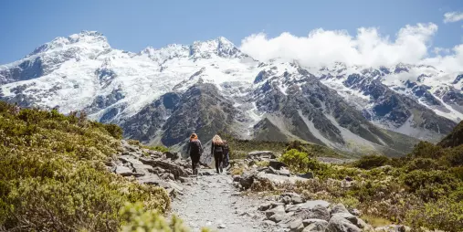 Two people hiking the Hooker Valley Track with Mount Sefton and Southern Alps behind.