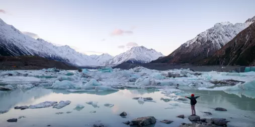 Person standing at the edge of Tasman Glacier Lake surrounded by floating icebergs.