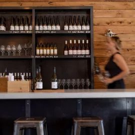 Mt Rosa Winery tasting room with wooden shelves of wine bottles and a staff member preparing glasses