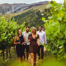 Small group walking through the vines with glasses of wine, surrounded by Central Otago hills