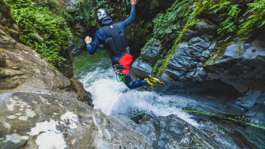 A canyoner jumps down a flowing waterfall into a plunge pool in a rugged Queenstown canyon.