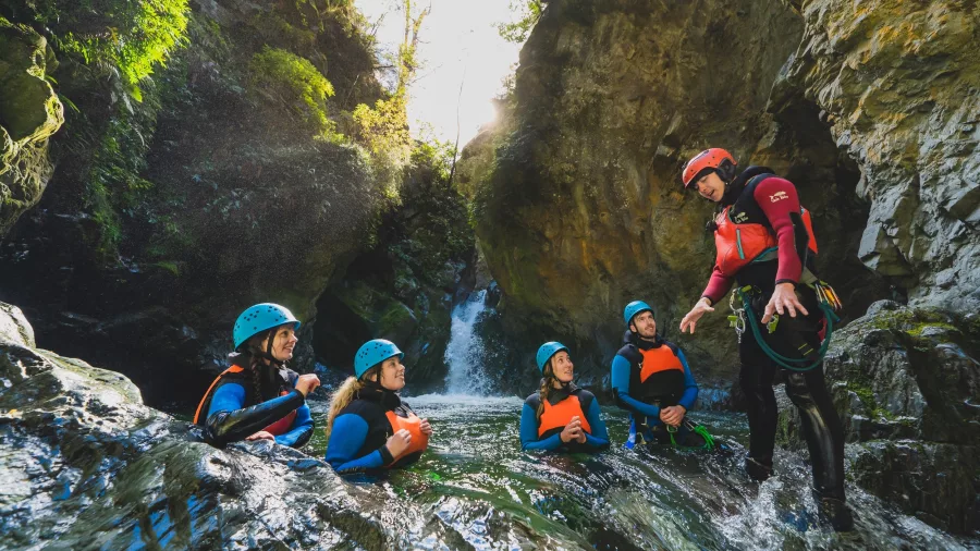 A canyon guide gives instructions to a group of participants standing in water near the canyon entrance, known as the Green Room.