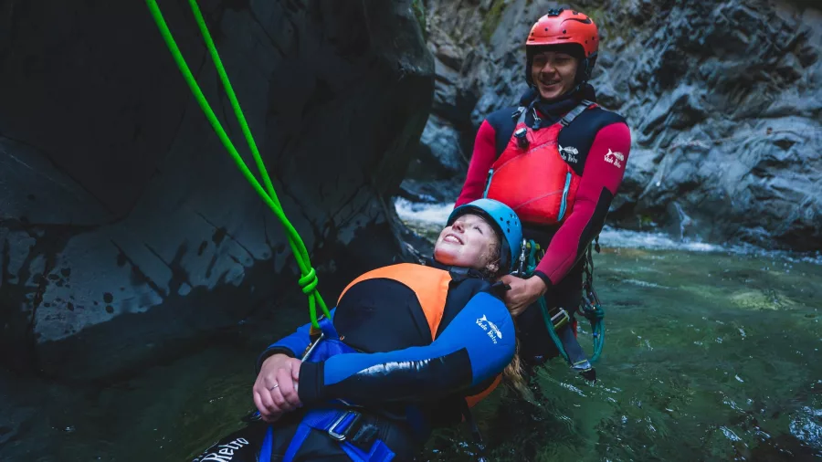 A guide supports a participant during a rope-assisted descent into a canyon pool in Queenstown.