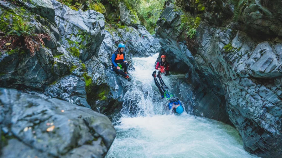 A canyoner slides down a steep rocky channel head first into fast-moving rapids during the Queenstown canyoning adventure.