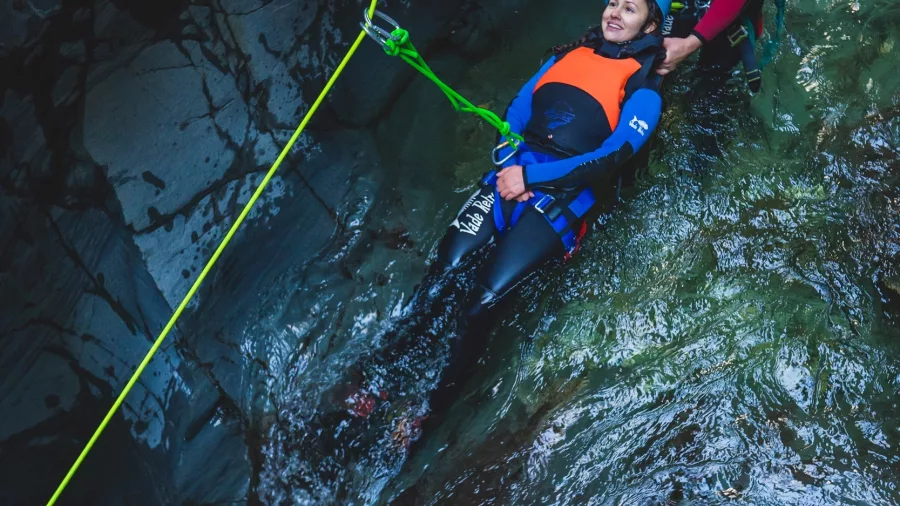 A canyon guide assists a participant using ropes during a descent beside a waterfall in a Queenstown canyon.