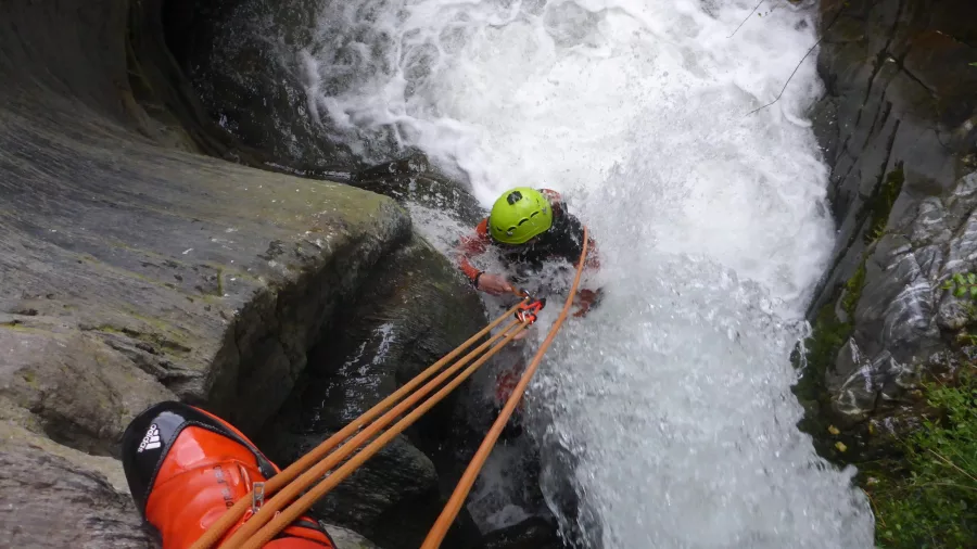 A canyoning participant abseils down a waterfall in Gibbston Valley, holding onto orange ropes as white water rushes below.