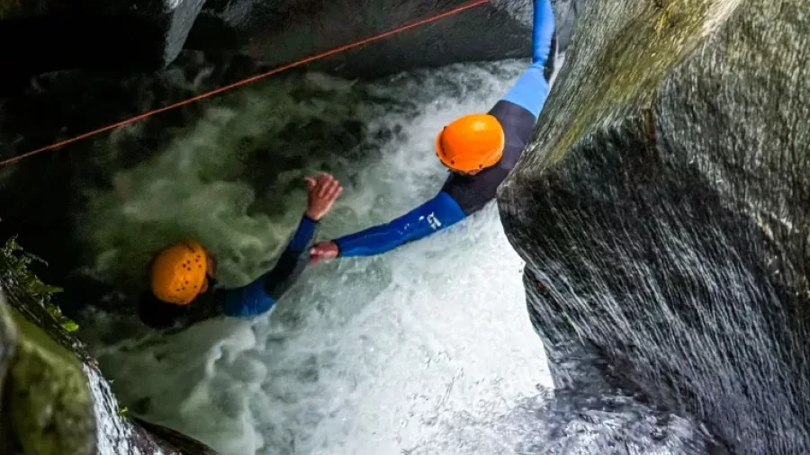 Canyoner helping another across narrow canyon water chute