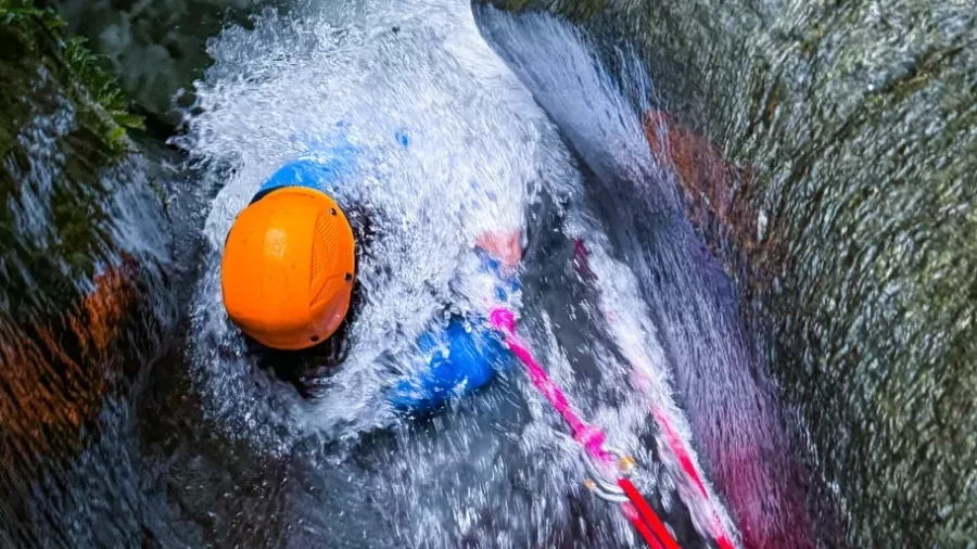 Canyoner sliding through strong waterfall using safety ropes