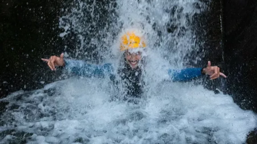 Canyoner standing under strong waterfall in canyon