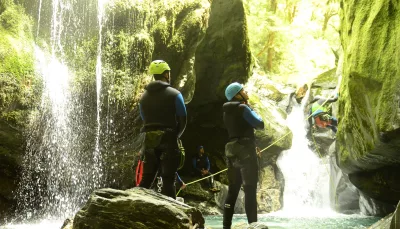 Two canyoners watch a teammate abseiling into a canyon pool beside a waterfall.