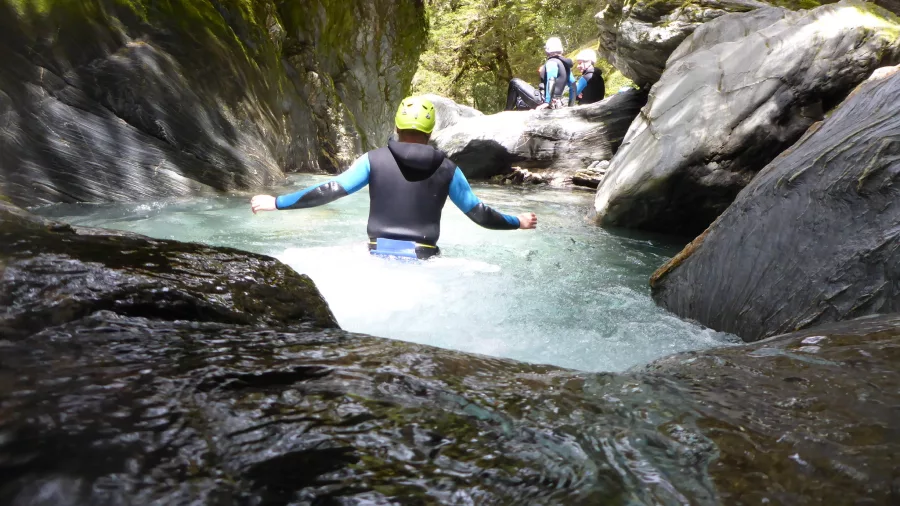 A canyoner wades through cool turquoise waters between dramatic canyon rock walls.