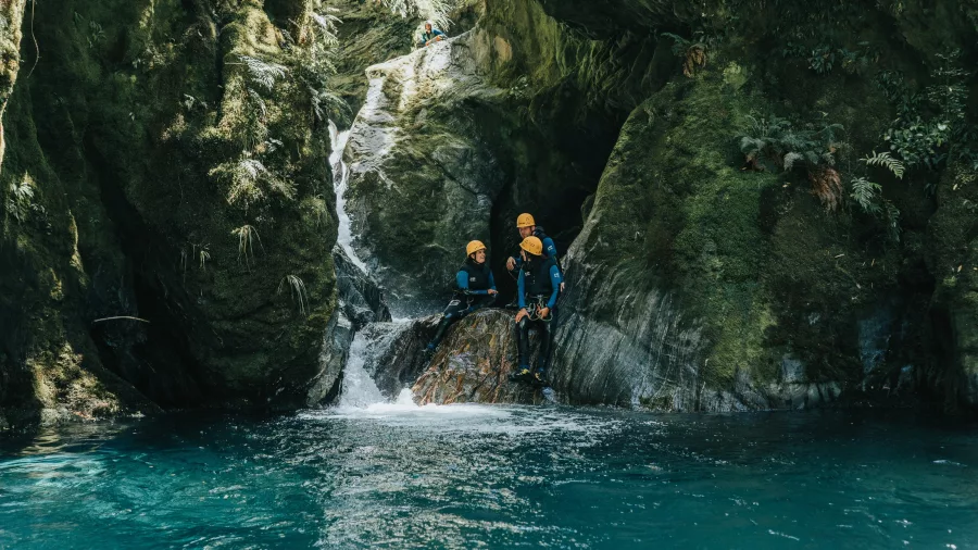 Three canyoners stand at the base of a waterfall, preparing to enter a turquoise canyon pool.