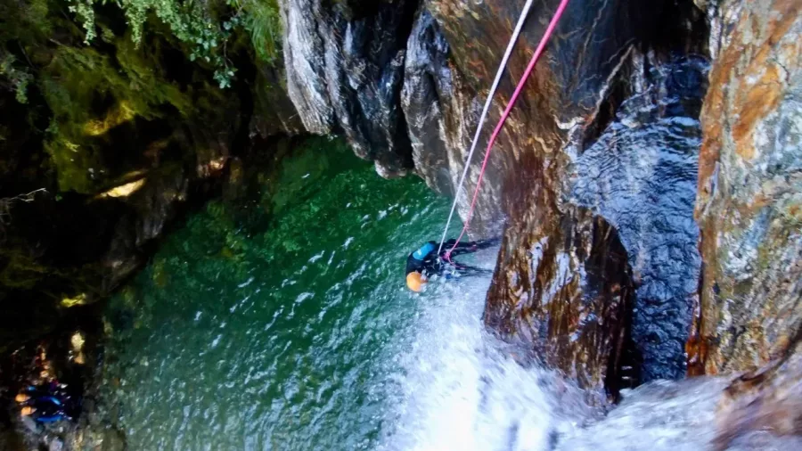 Canyoner abseiling down wet rock wall into green canyon pool