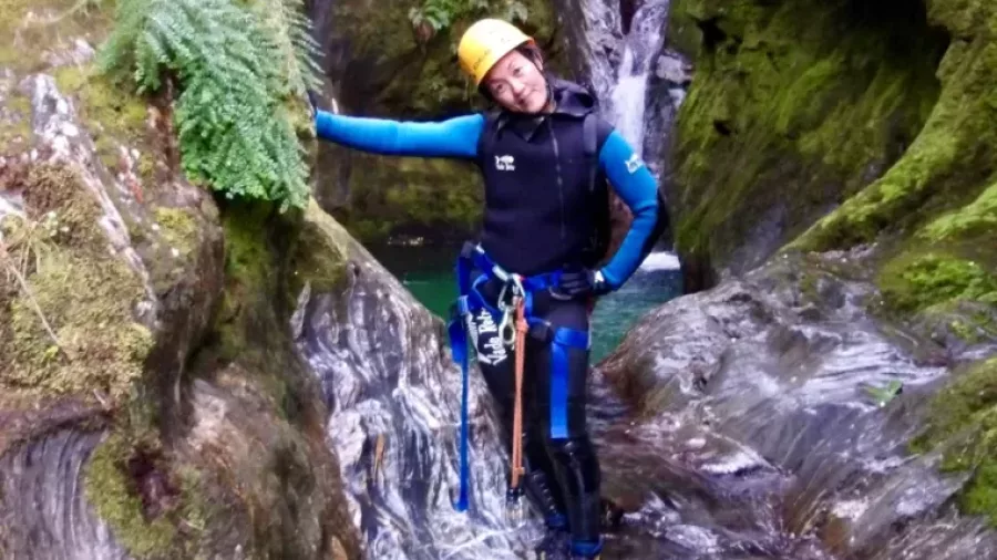 Canyoner posing beside mossy canyon wall near water