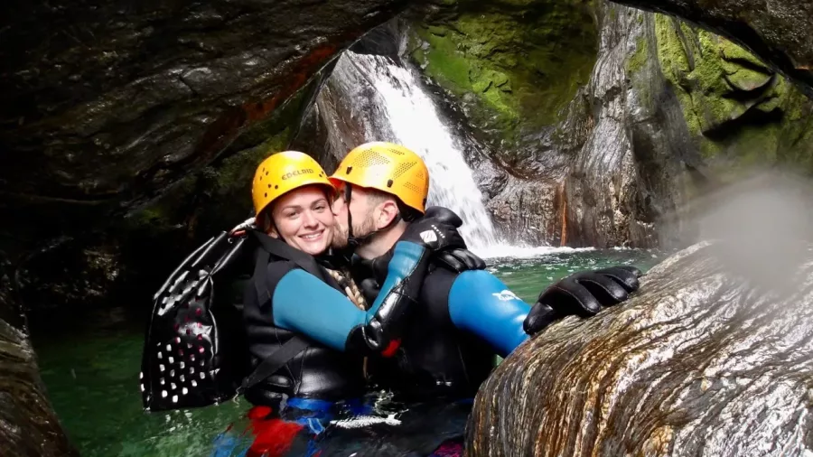 Couple kissing under rock arch in canyon with waterfall backdrop