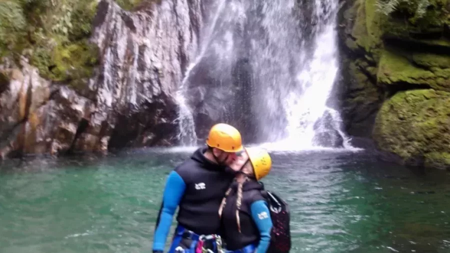 Canyoning couple standing together in front of waterfall