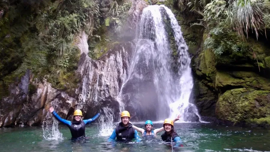 Four canyoners smiling in pool below waterfall in Mt Aspiring