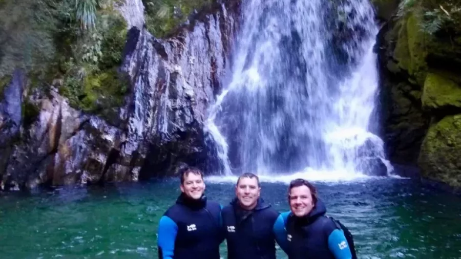 Three canyoners posing in front of a waterfall in Mt Aspiring