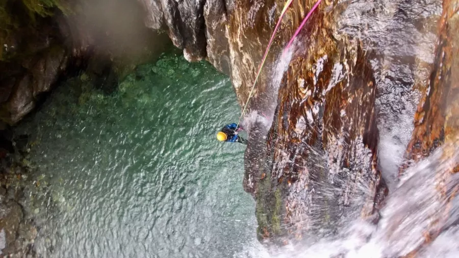 Canyoner abseiling down cliff into emerald canyon pool